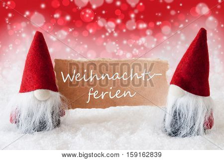 Christmas Greeting Card With Two Red Gnomes. Sparkling Bokeh And Christmassy Background With Snow. German Text Weihnachtsferien Means Christmas Break