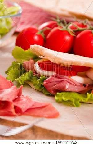 Piadina with ham and lettuce on wooden table.