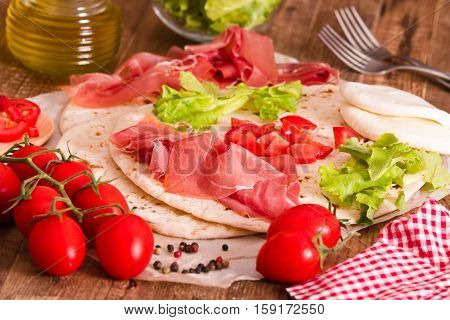 Piadina with ham and lettuce on wooden table.