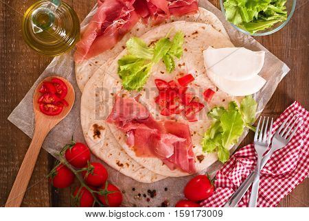 Piadina with ham and lettuce on wooden table.