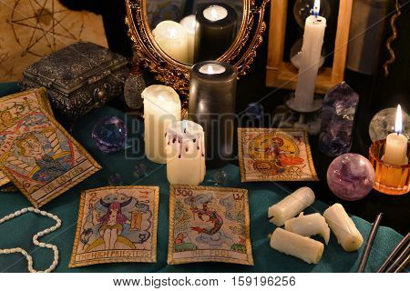 Magic still life with crystals, the Tarot cards and candles reflected in mirror. Halloween concept, mystic fortune telling ritual with occult symbols, divination rite. Vintage objects on witch table