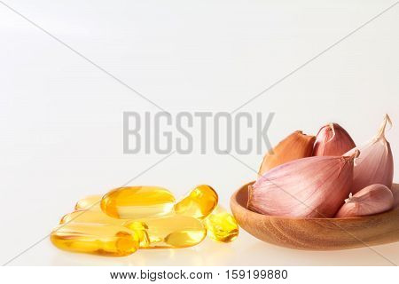 Close up garlic and oil capsule gel supplement in a wooden spoon on white background healthy vitamin supplement from garlic oil concept
