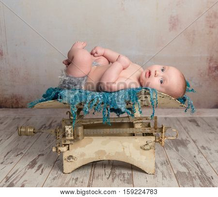 cute little baby with legs up lying on child scales on wooden floor