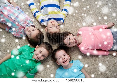 christmas, winter holidays, childhood, friendship and people concept - group of happy smiling little children lying on floor and holding hands over snow