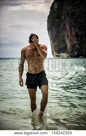 Half body shot of a handsome young man standing on a beach in Phuket Island, Thailand, shirtless wearing boxer shorts, showing muscular fit body