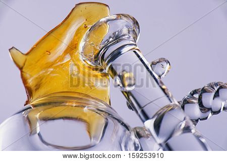 Close up view of a piece of cannabis oil concentrate aka shatter with glass rig bowl and nail isolated on white