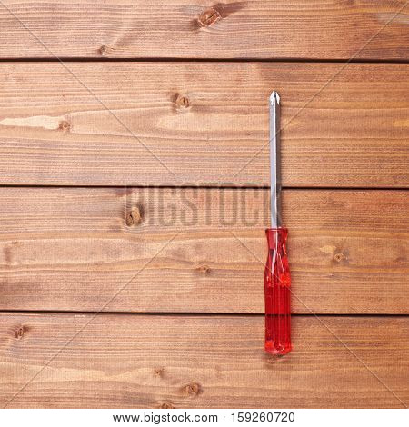 Cruciform screwdriver with the red handle on wooden brown surface