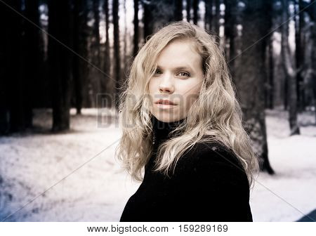 portrait of a woman with blond curly hair on the background of the winter forest, processed photo in shades of brown, bright woman with alluring and attractive look, languid, snowing,