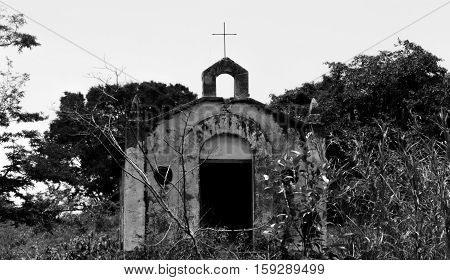 Old small chappel deteriorated by time surrounded by woods inspiring dark mood B&W