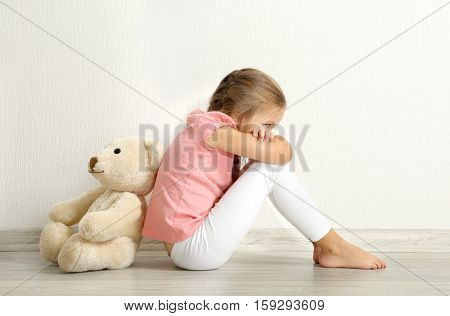 Sad little girl with teddy bear sitting on floor in empty room