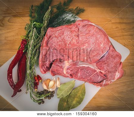Fresh raw beef on wooden cutting board, spices and herbs. Whole uncooked beef prepare for cooking. Large piece of fresh beef ham.