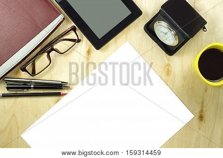 Office table desk top view with tablet PCa cup of coffee pen pencil glasses clock book and blank paper on wooden background.