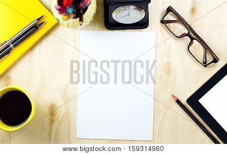 Office table desk top view with tablet PCa cup of coffee pen pencil glasses clock book and blank paper on wooden background.