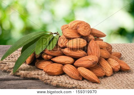 heap of peeled almonds with leaf on a wooden table with blurred garden background.