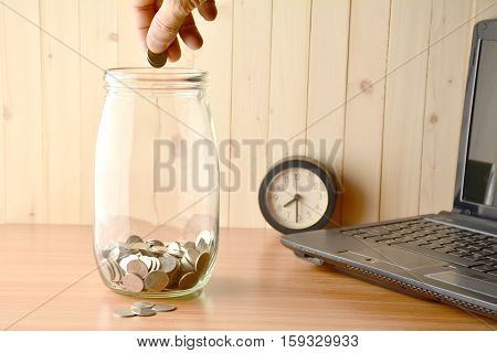 Men drop coin into the bottle, alarm clock and laptop on the table.