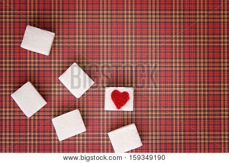 Sugar cubes with a red heart on one of them as background. Top view. Diet unhealty sweet addiction concept