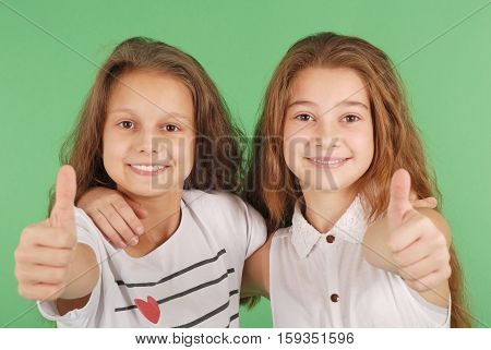 Two smiling young school girls showing thumbs up isolated on green background