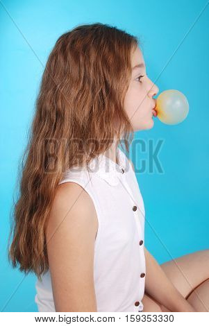 Young girl doing bubble with chewing gum blue background