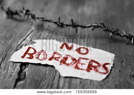 closeup of a barbed wire and a piece of paper with the text no borders handwritten in it on a rustic wooden surface