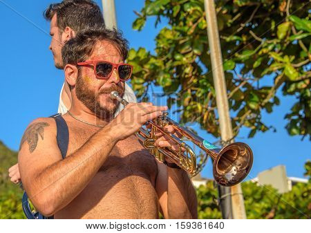 27 November, 2016. Man in sunglasses with tattoo of turtle playing trumpet in the street at sunny day at Festival de Fanfarras Ativistas - HONK RiO 2016 at Leme district, Rio de Janeiro, Brazil