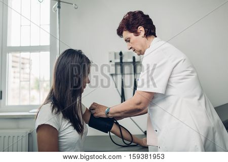 General practicioner measuring her patient's heart pressure and smiling to patient. Interacting and taking care of patient. Taking care of your health. Disease prevention.