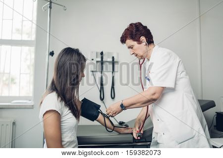 General practicioner measuring her patient's heart pressure and smiling to patient. Interacting and taking care of patient. Taking care of your health. Disease prevention.