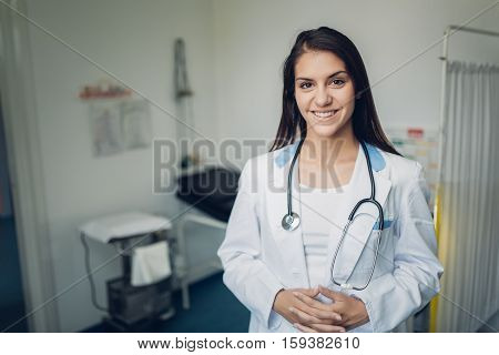 Portrait of a confident young female doctor standing in her office, smiling at camera. Health care and prevention concept. Friendly and approachable medical care from practicioner.