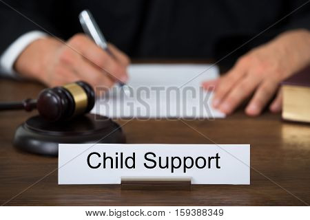 Close-up Of Nameplate Displaying Child Support And Legal Gavel On Wooden Desk In Court