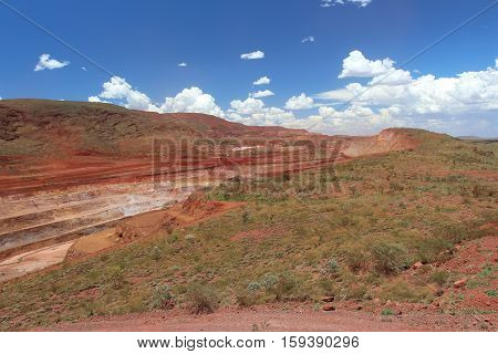 One of the many long strip open cut pits at at Tom Price iron ore mine in the Pilbara region of Western Australia.  Blending in with the natural landscape on either side.