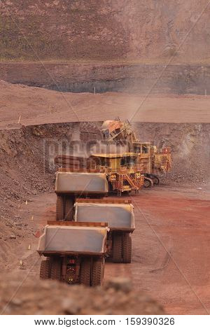 A Yellow XE-MC haul truck, first in a long queue being loaded with waste rock at the Tom Price iron ore mine in the Pilbara region of Western Australia