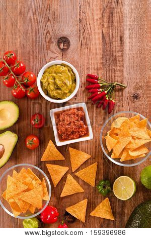 Guacamole and nacho chips on wooden table.