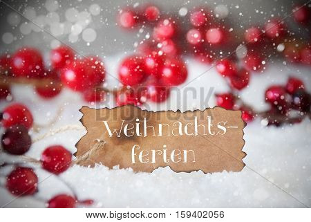 Burnt Label With German Text Weihnachtsferien Means Christmas Break. Red Christmas Decoration On Snow. Cement Wall As Background With Bokeh Effect And Snowflakes. Card For Seasons Greetings