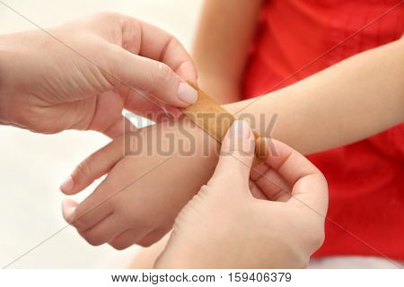 Woman applying sticking plaster to little girl's wrist, close up view