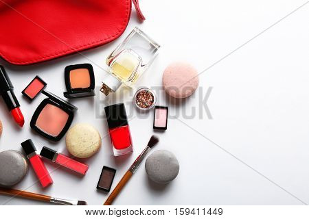 Makeup products with cosmetic bag and macaroons on light background
