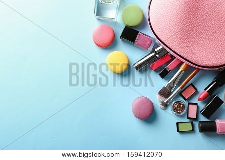 Makeup products with cosmetic bag and macaroons on blue background