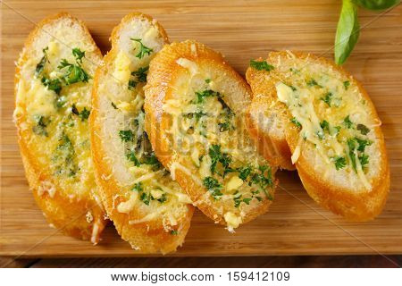 Tasty bread with garlic, cheese and herbs on wooden kitchen board, close up