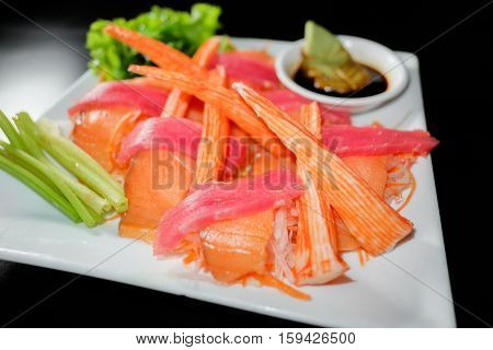 Tuna sashimi and crabstick with soy sauce on black background