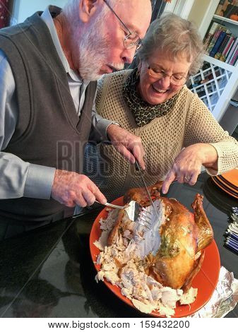 Senior Adult Couple Cutting the Holiday Turkey Together In The Kitchen.