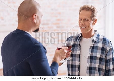 We drinking wine . Smiling involved cheerful non-traditional couple standing in the bedroom and drinking wine while expressing happiness and having conversation