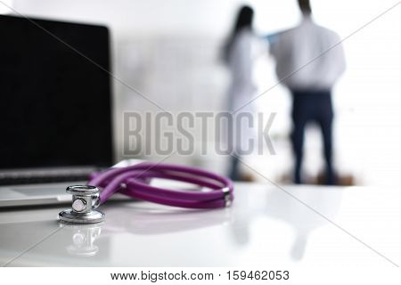 Laptop and stethoscope on the desk , doctors standing in the background.