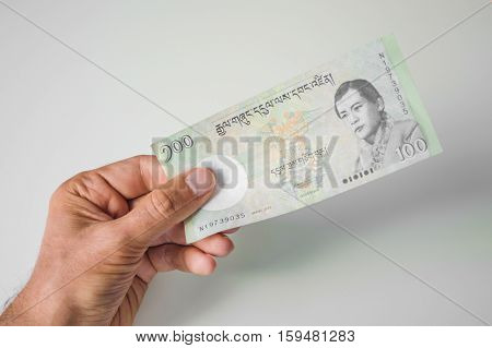 Man Holding Hundred Bhutanese Ngultrum Banknote In His Hand