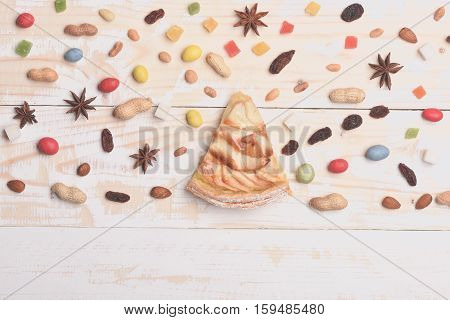 Single slice of apple pie with mix of colorful dragee marmalade or jelly candies almonds peanuts raisins anise sugar cubes on vintage wooden background