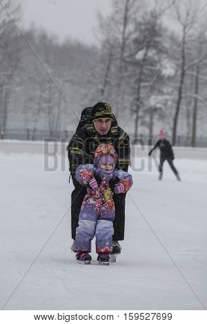 Saint-Petersburg Russia - December 2 2016: Urban outdoor ice rink in the park. Father teaching his child to skate.