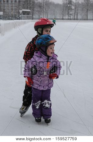Saint-Petersburg Russia - December 2 2016: Urban outdoor ice rink in the park. Two children skating on the ice.
