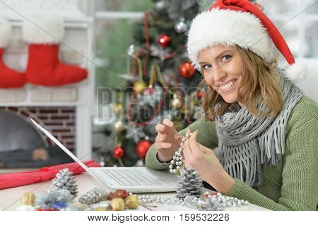 Portrait of young smiling woman in Santa hat preparing for Christmas, making hand made decoration