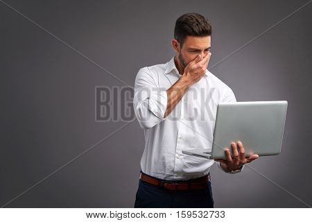 A handsome young man feeling confused while looking at a laptop in a white shirt