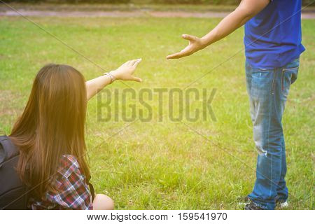 Woman sitting on the grass reaching to shake the hand of man. helping hand and love concept.