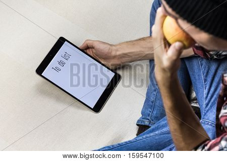 Eating an apple. Man bites apple and holds tablet PC with to do list sign