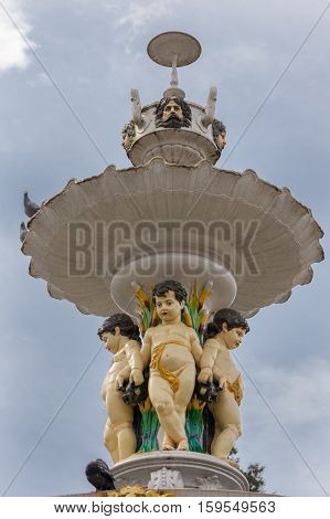 Nilgiri Hills India - October 25 2013: closeup of the top section of the 19th century Adam Fountain on Charring Cross Square in Ooty. Shows three painted angels adam faces circular plateaus under light blue sky.