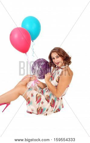 A beautiful young woman sitting on the floor holding two balloons and a lollypop isolated for white background.
